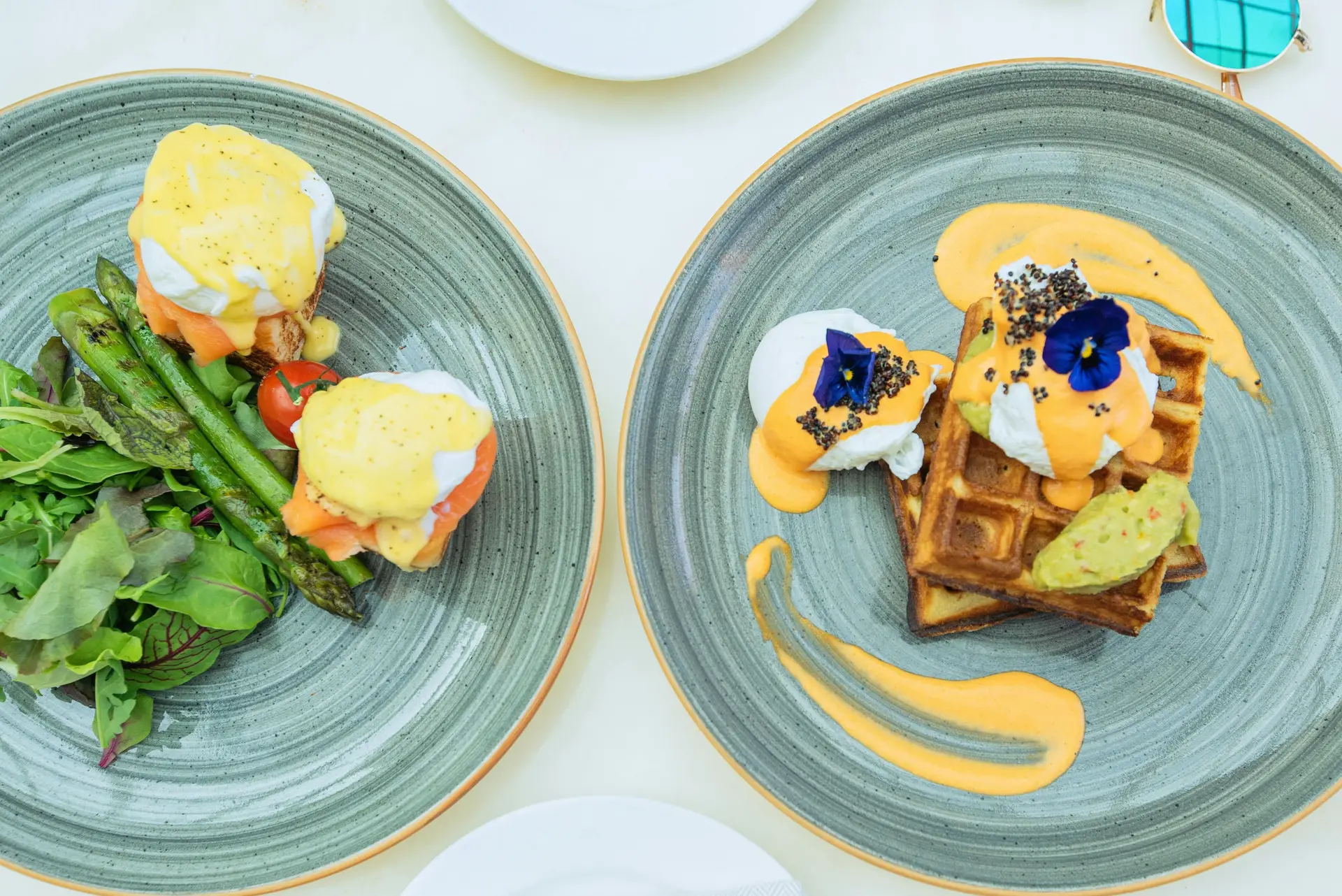 Waffles with hollandaise sauce, eggs and salad served on two green plates.