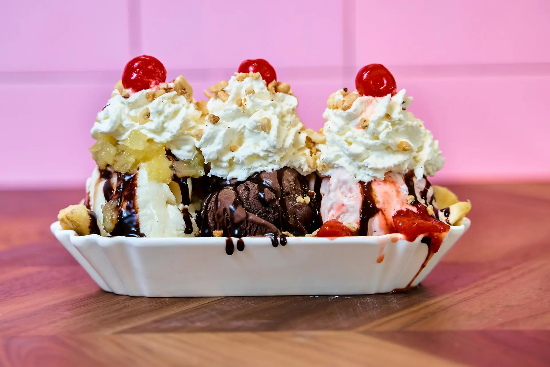 A banana split topped with whipped cream, cherry, chocolate syrup, etc, in a plate.