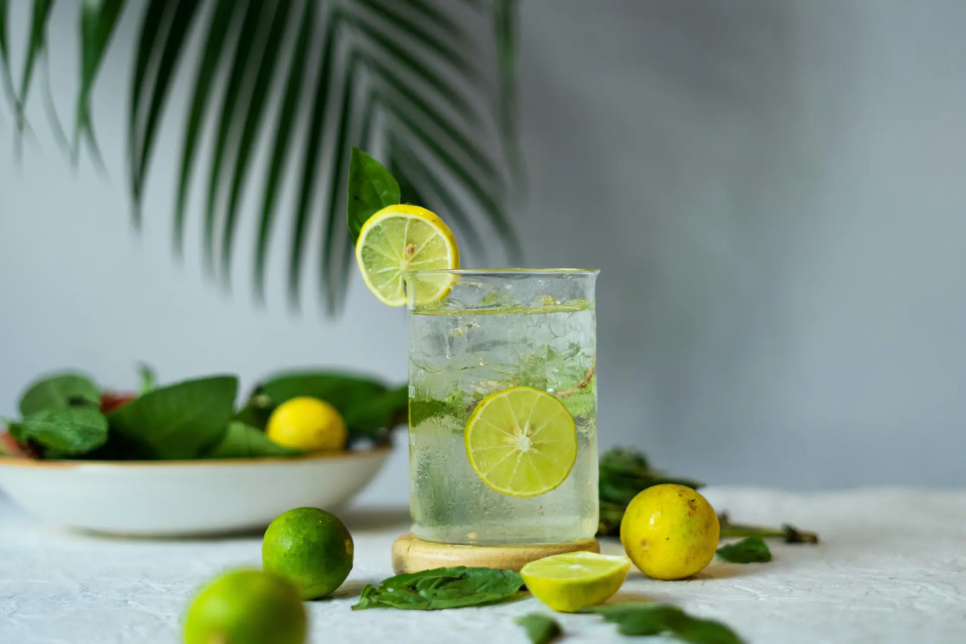 A glass of lemonade with lemon in it. There are some lemons in a bowl near the glass as well.