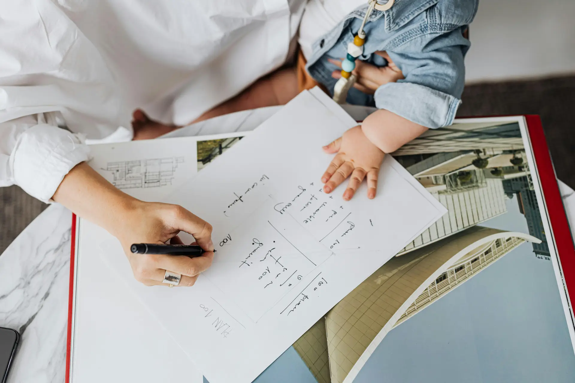 A person writing on a paper while a child is putting its hand on the paper.