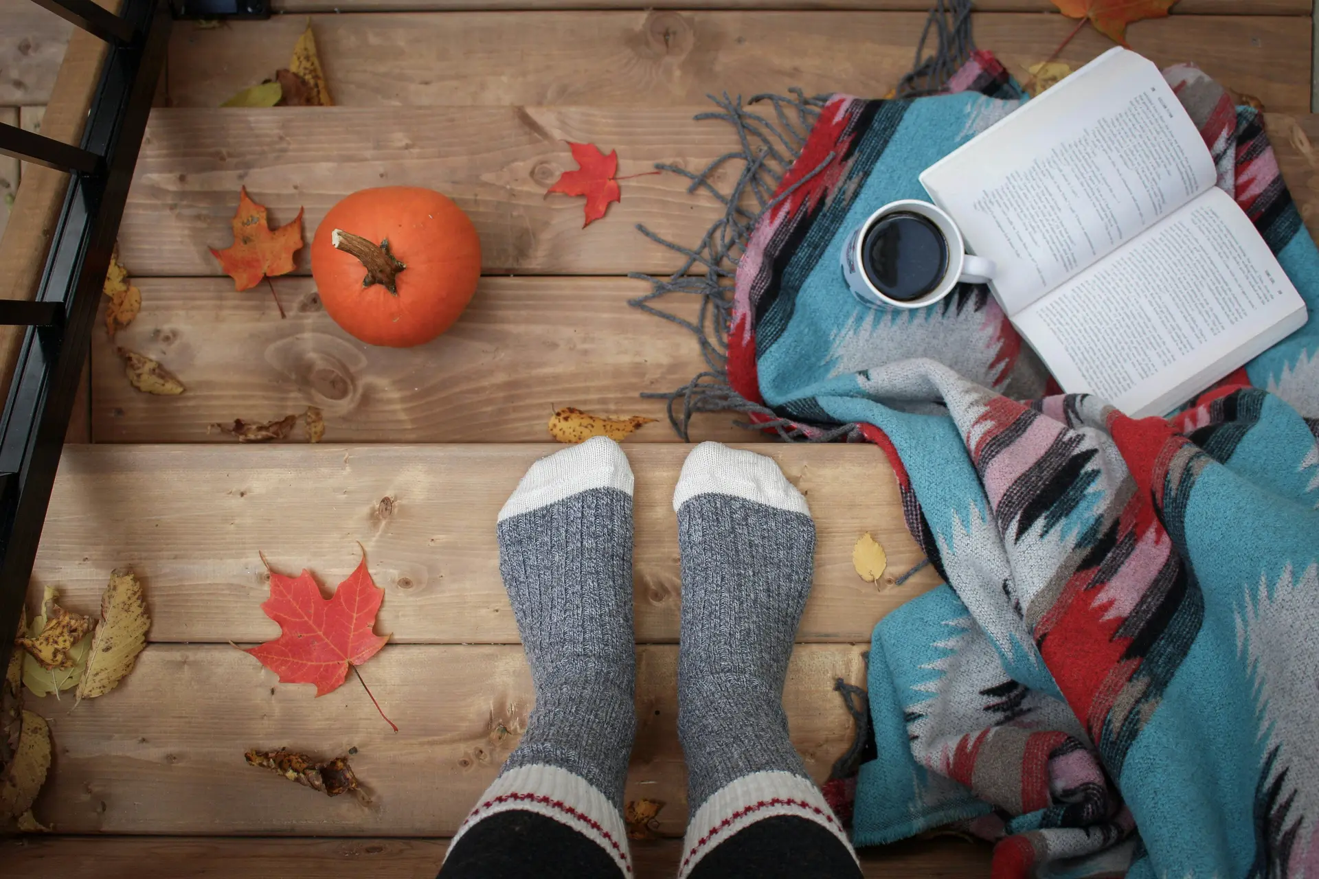 A person wearing gray sock standing on stairs. On the stairs there is a book, a cup of coffee, and a pumpkin.
