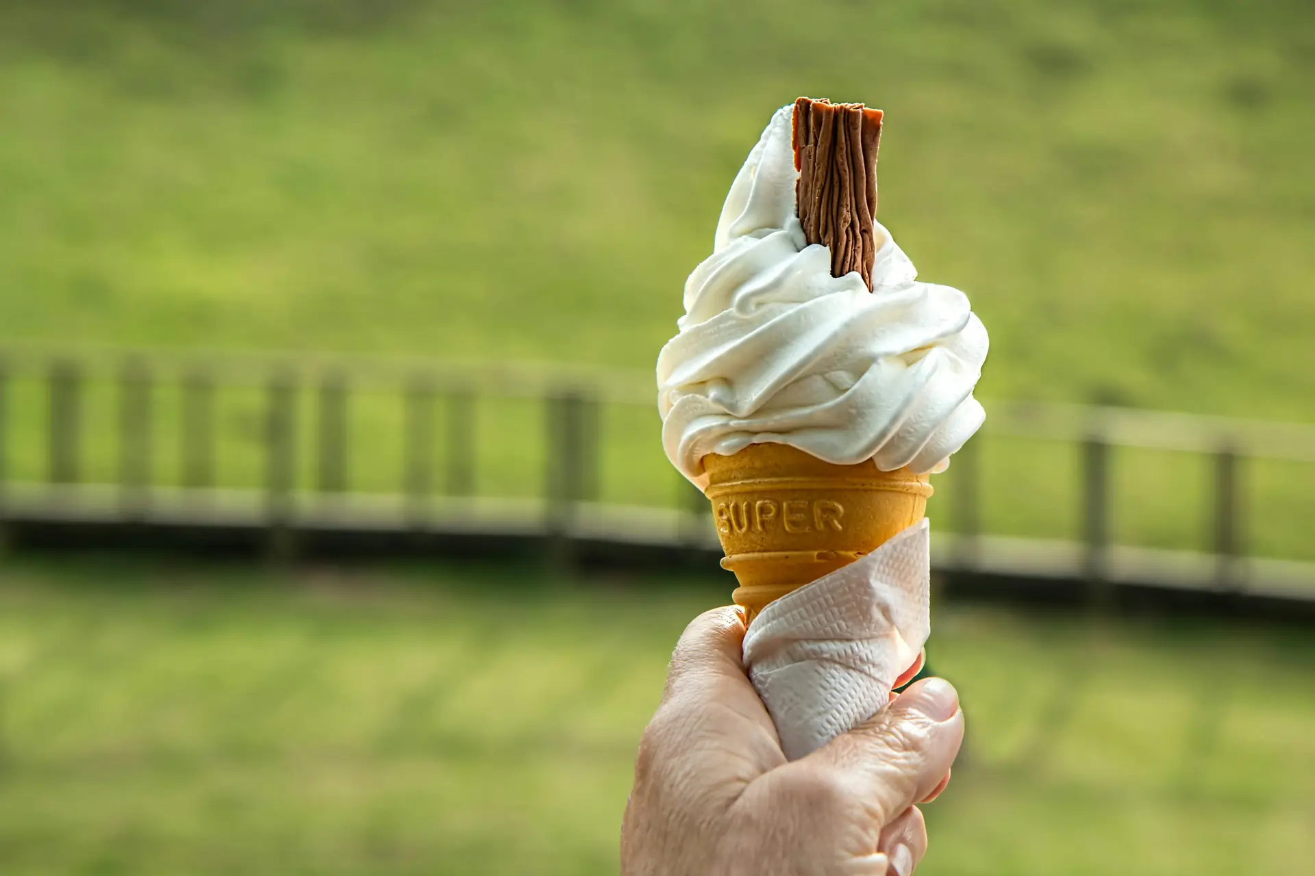 Vanilla ice cream cone held by a person whose hand is only visible.