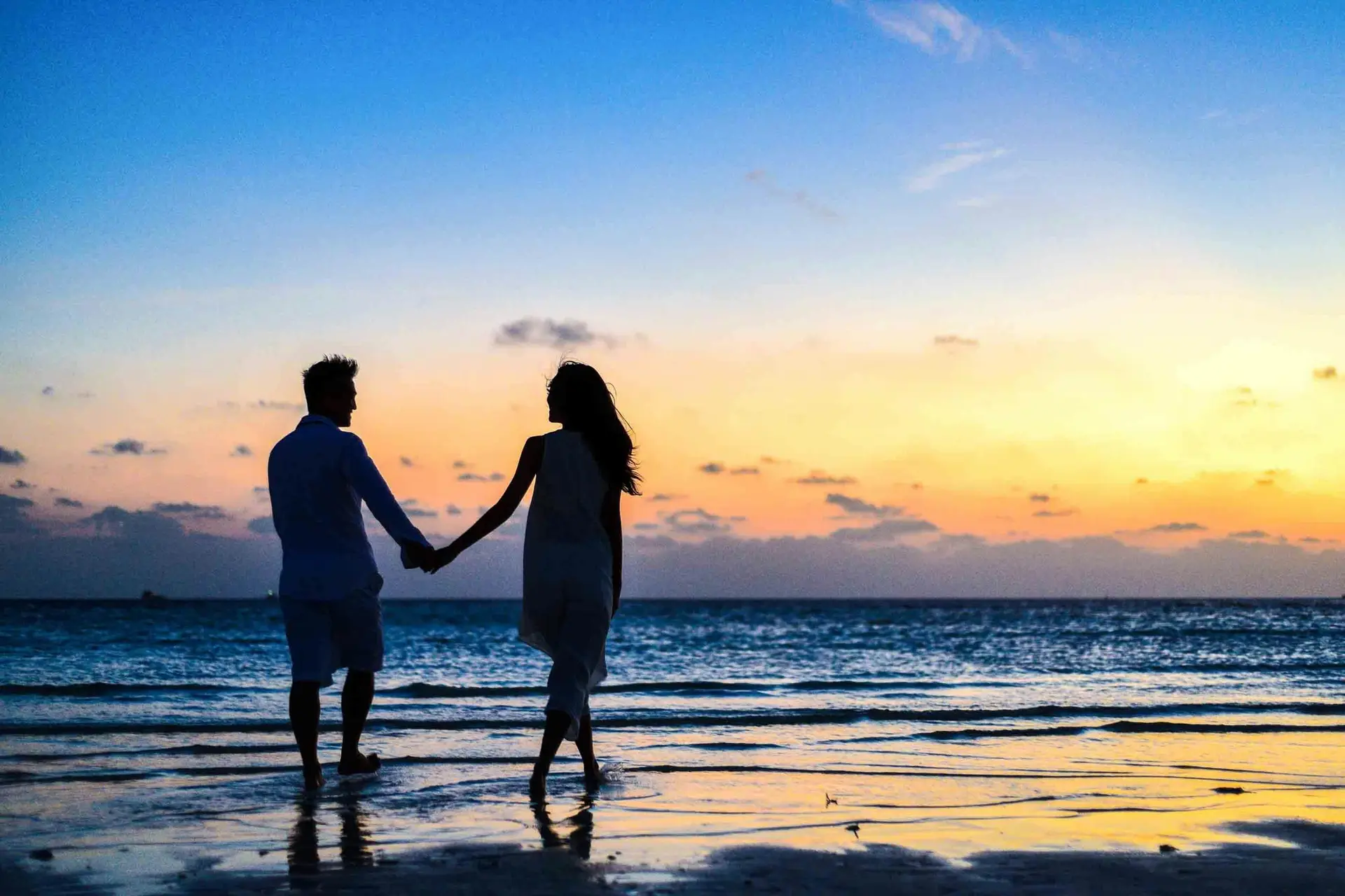 A couple holding hands on the beach as the sun sets.