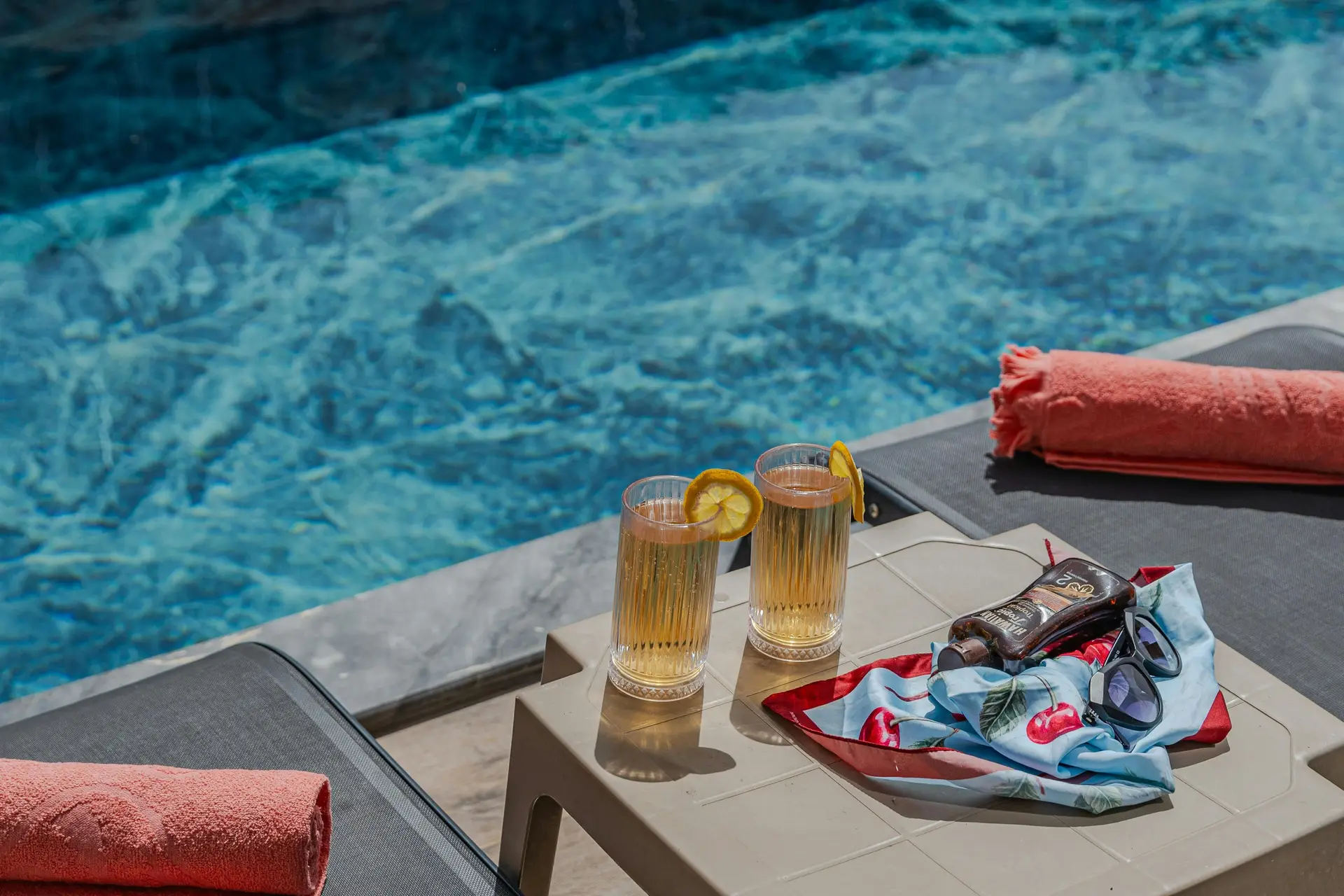 A pair of sunglass near a pool. Its placed on a small pool table with two glasses of drinks.