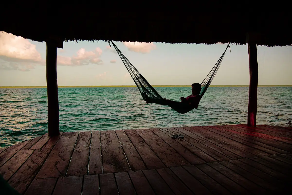 A person relaxing in a hammock over Bacalar Lagoon's tranquil waters.