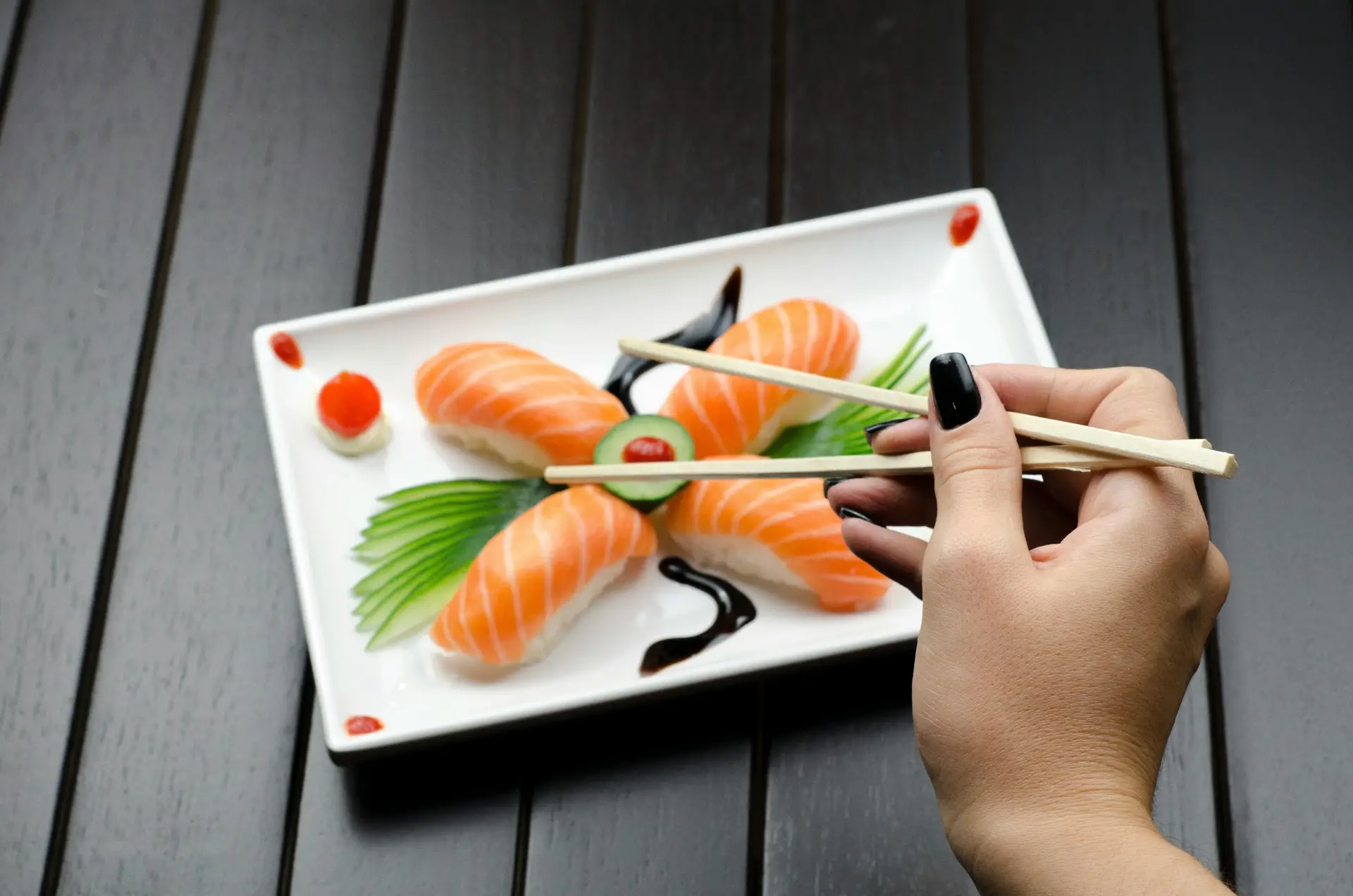 Person picking up sushi rolls with chopsticks from a plate.