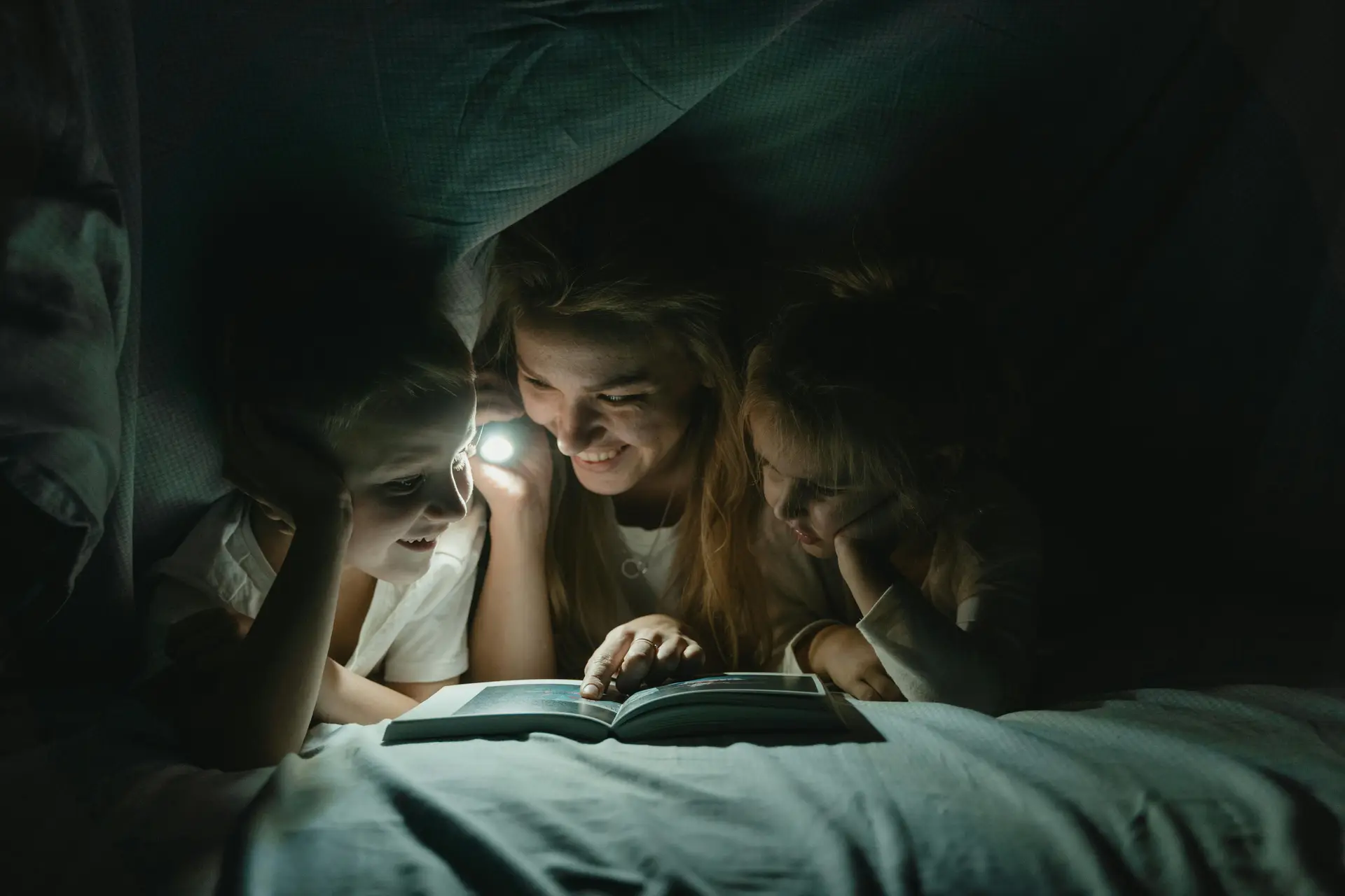 Woman Telling a Story to children under the blanked while holding the light.