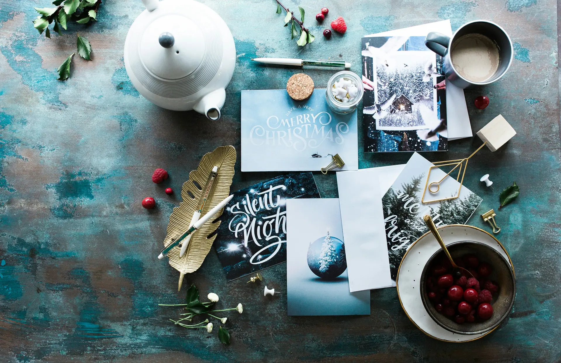 Different items such as teacup, teapot, fruits, leaves assorted on a table with greeting cards and pens to write on the cards.