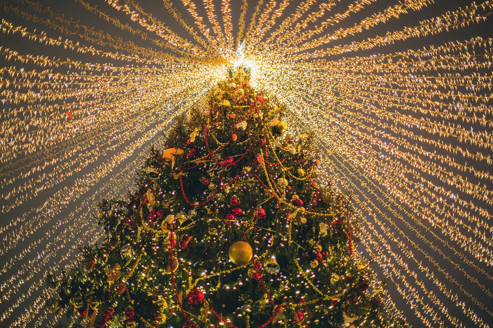 A brightly lit christmas tree. It is adorned with various decorations, including string lights, small toys, dolls, paper ornaments, lanterns, and others.