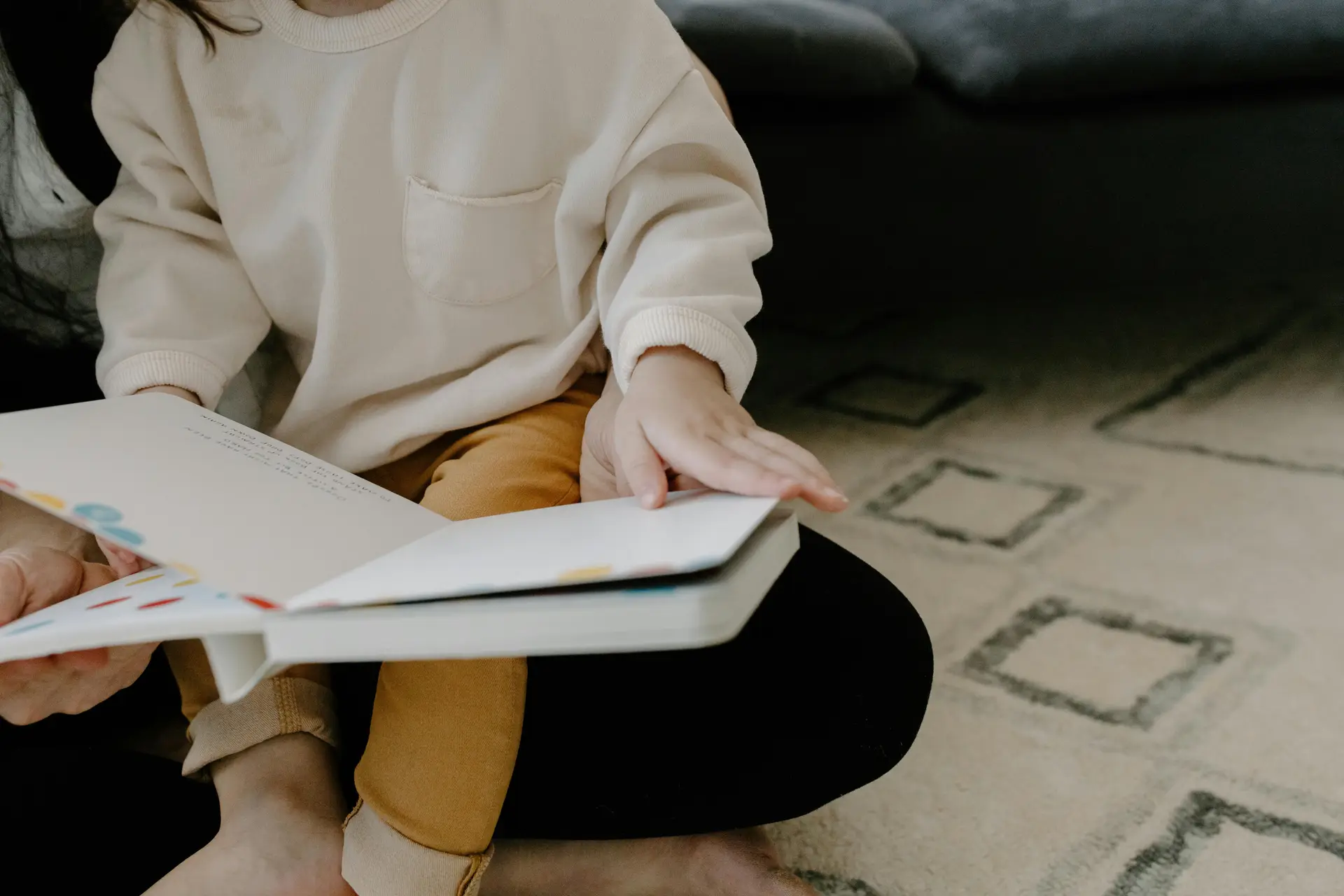 A child on a lap of a person flipping through a storybook.