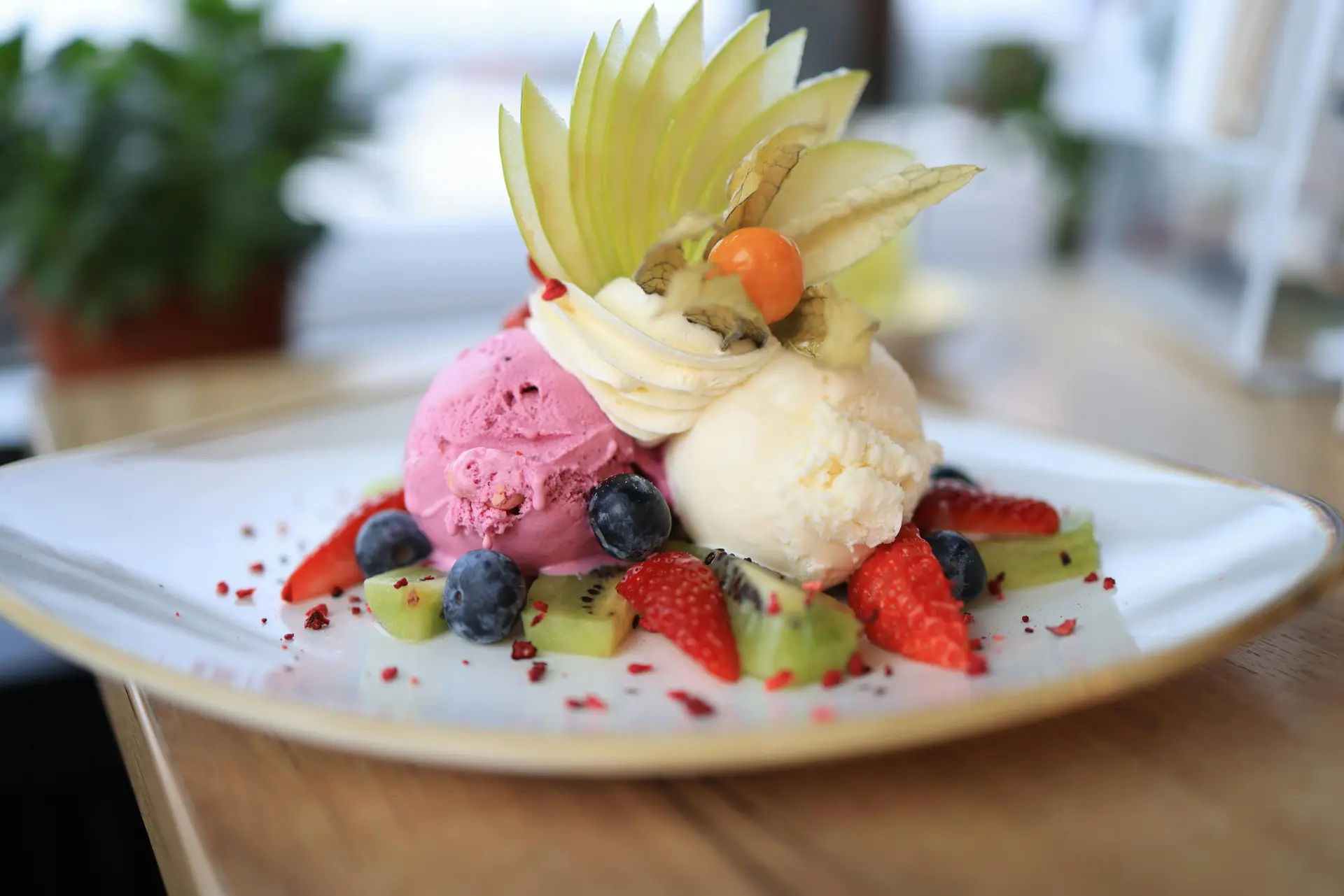 Exclusive vanilla ice cream dessert presented with fruits and scoops of strawberry ice cream.