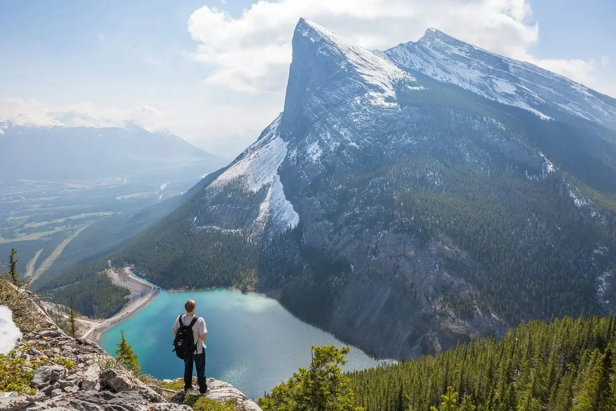 A person standing in front of lake under a big mountain with icy peaks.