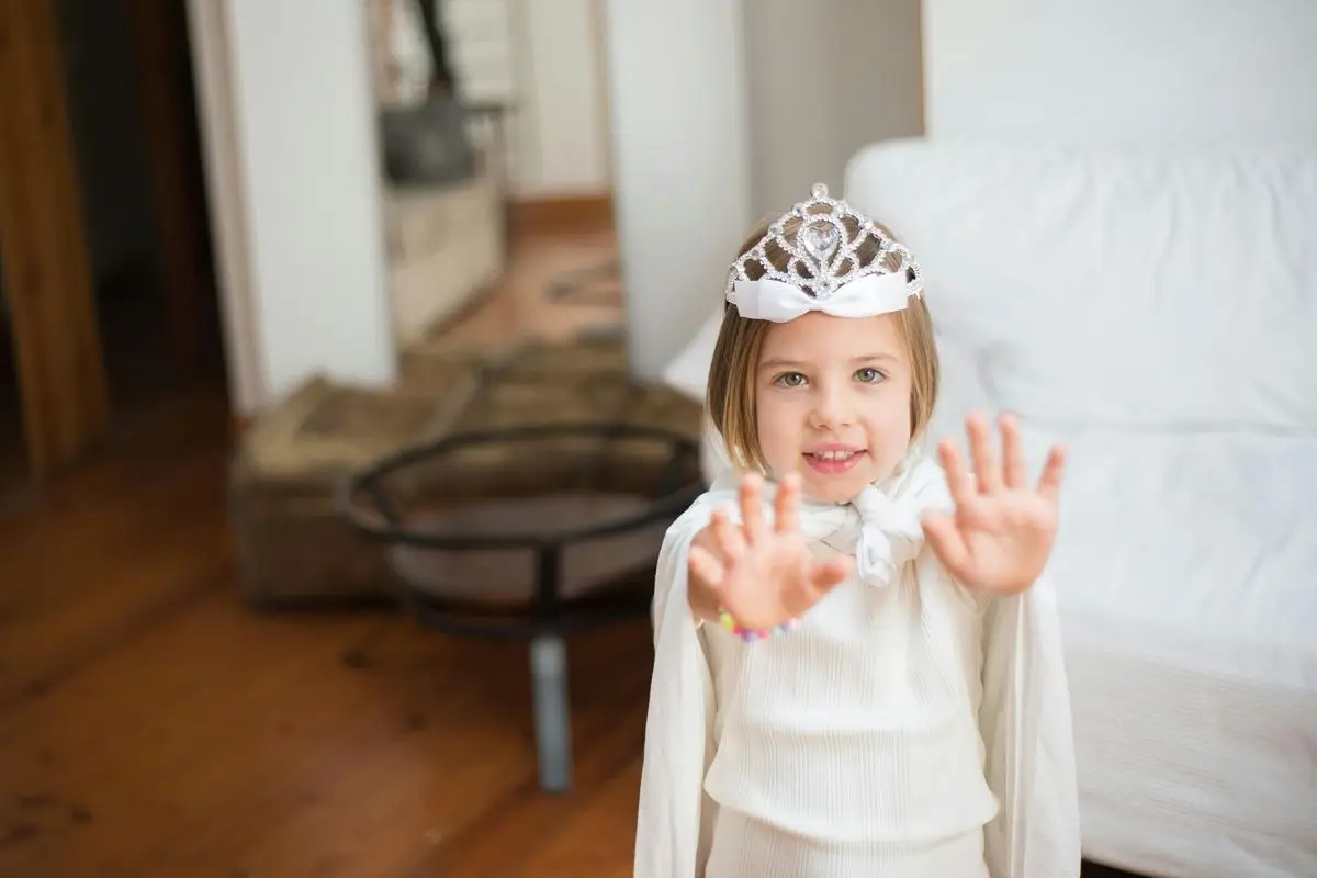 A child wearing a white princess dress along with a tiara.