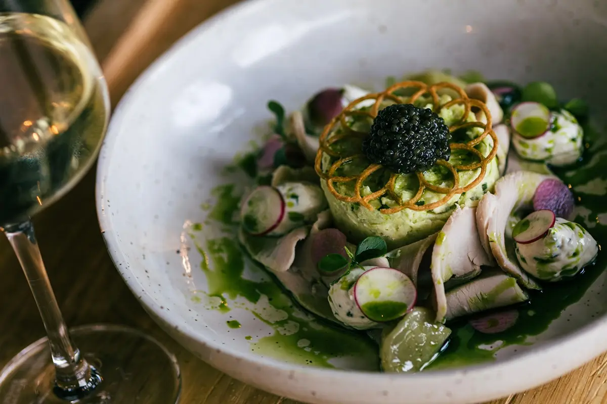 Elegant gourmet dish featuring caviar, served with white wine in a refined restaurant setting.