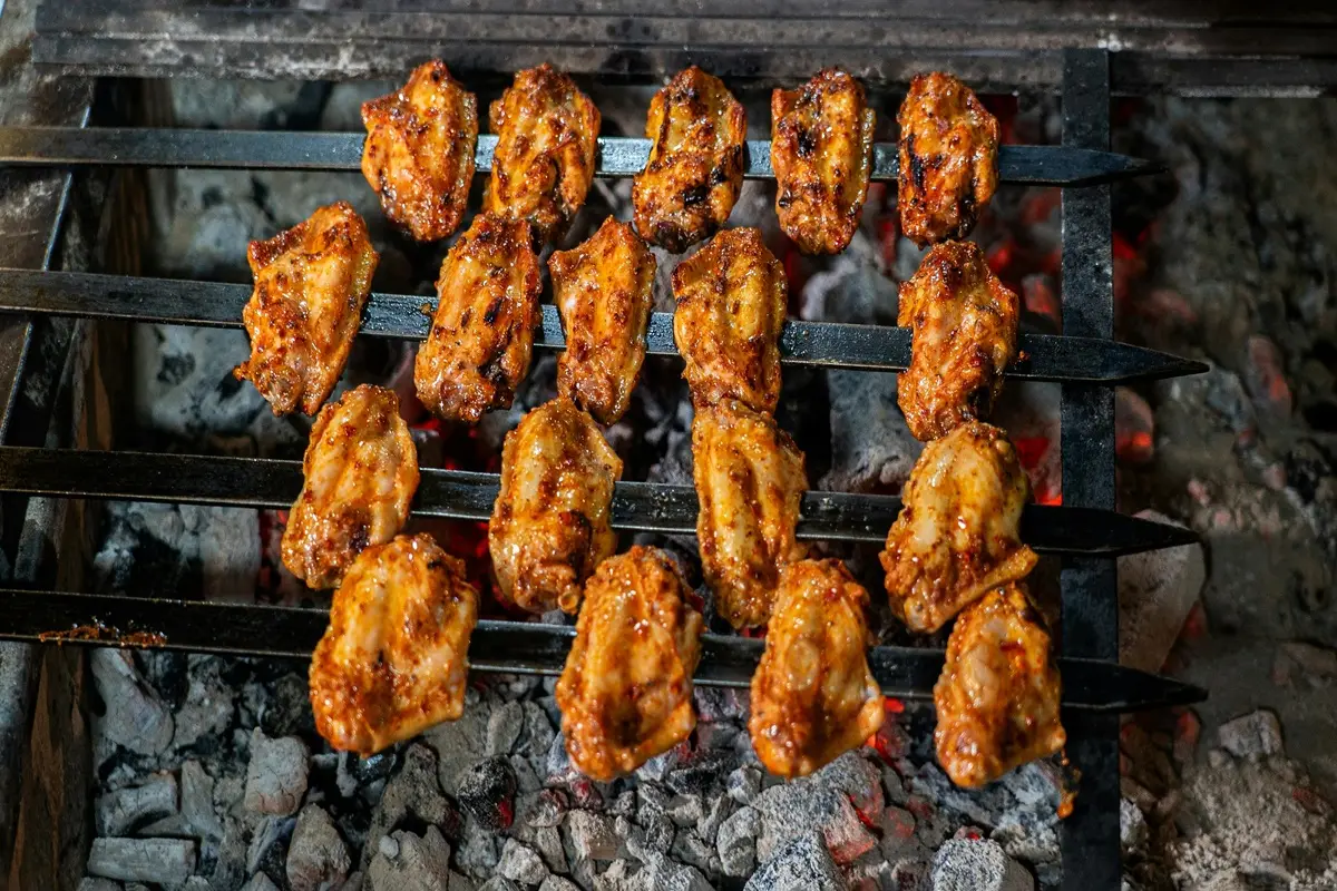 Juicy grilled chicken wings on skewers sizzling over a charcoal grill, perfect for a barbecue.