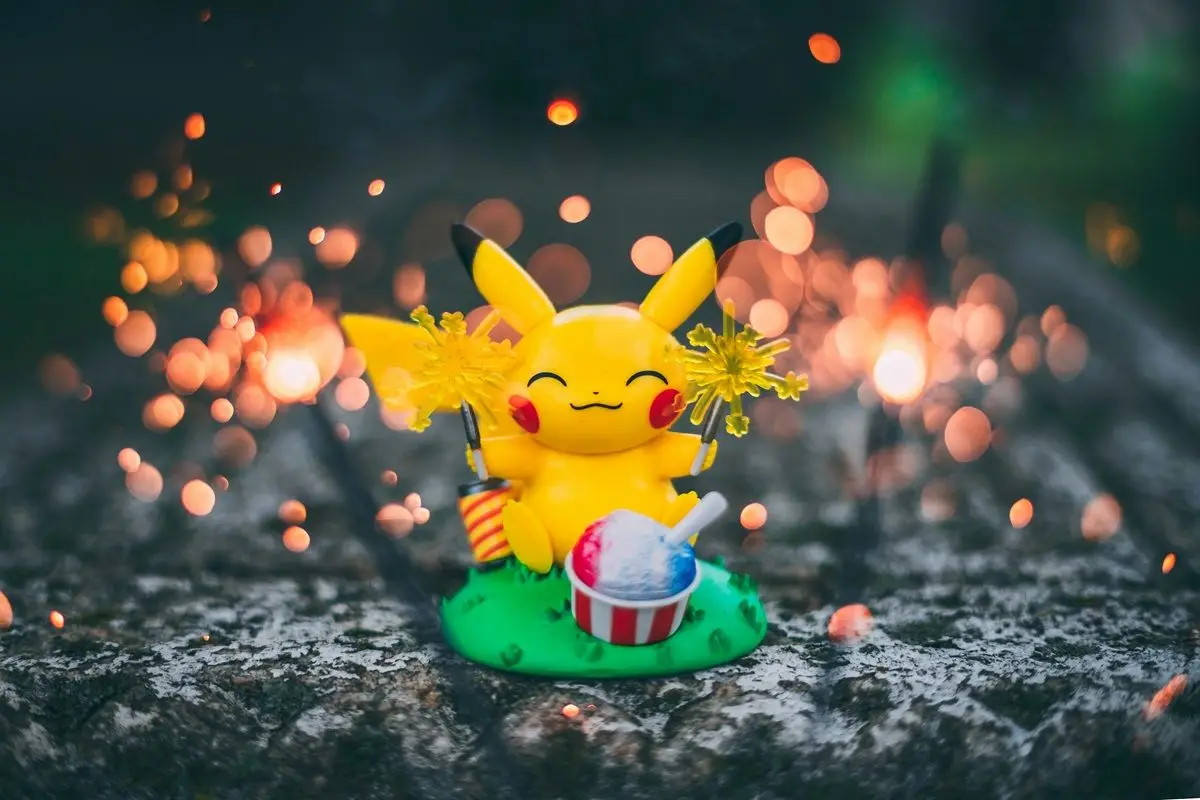 A pikachu doll on the ground with a cake front of it placed on the ground.