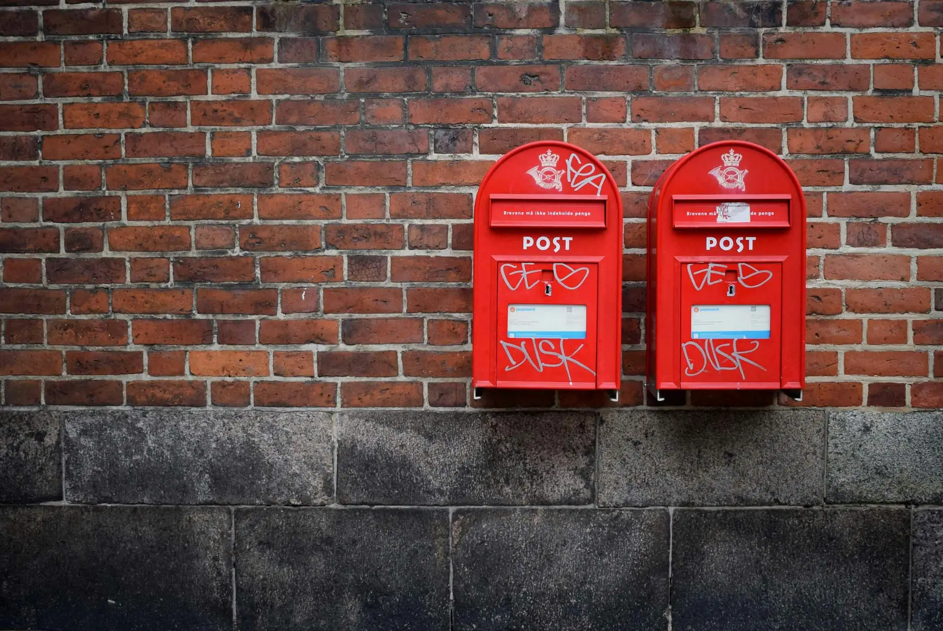 Two red post boxes mounted in brown concrete wall.