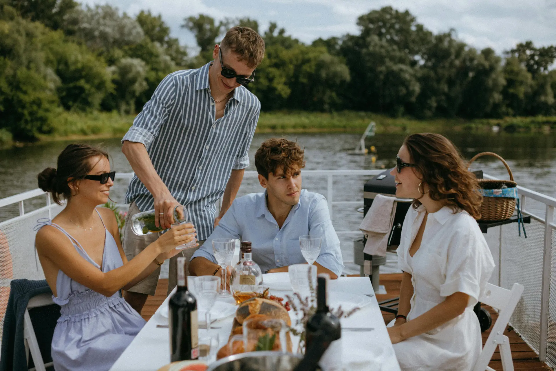 Two men and two women having lunch on a boat in a river. One man is serving drinks to a woman's glass.