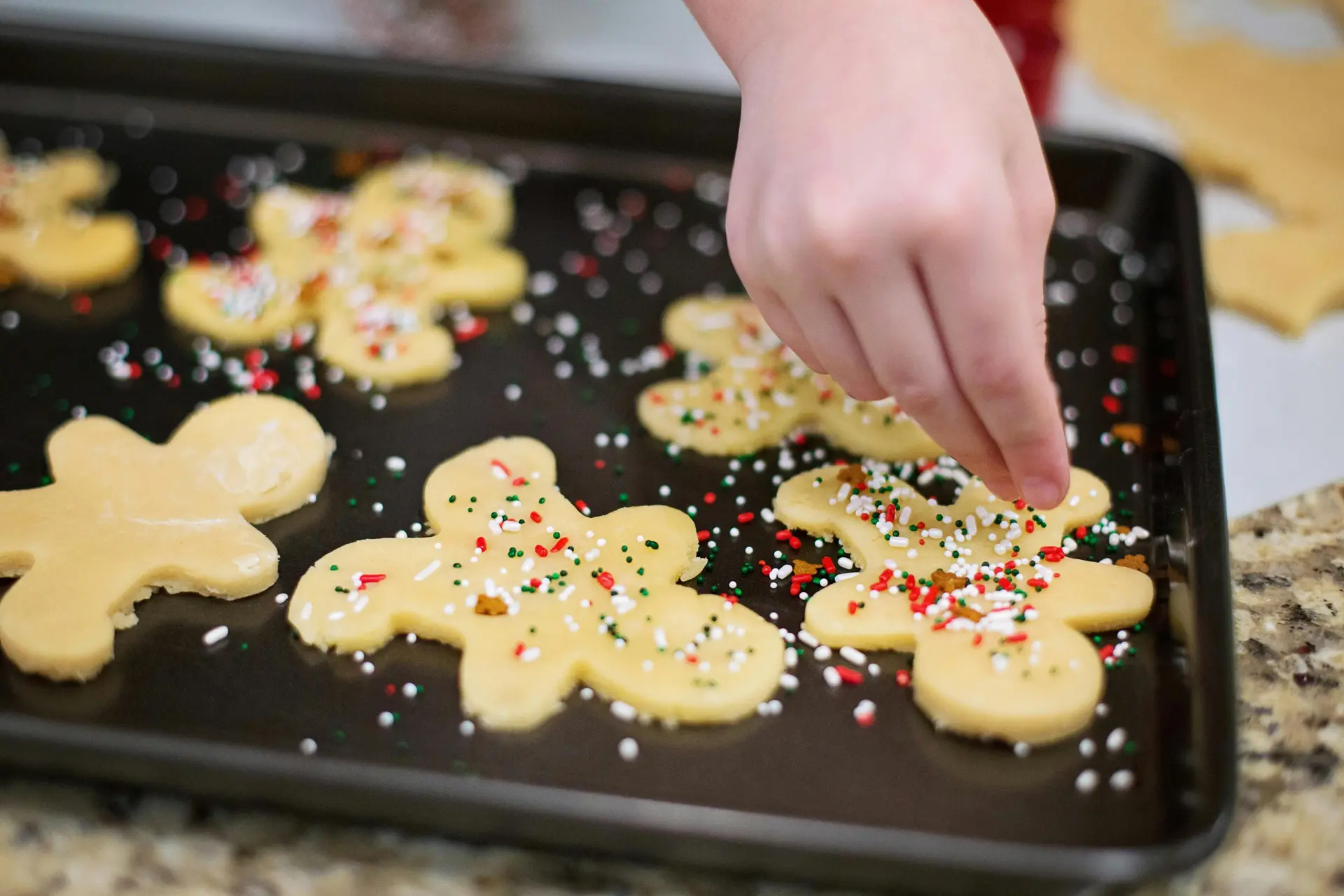 A person decorating Christmas cookies on a tray with sprinkles.