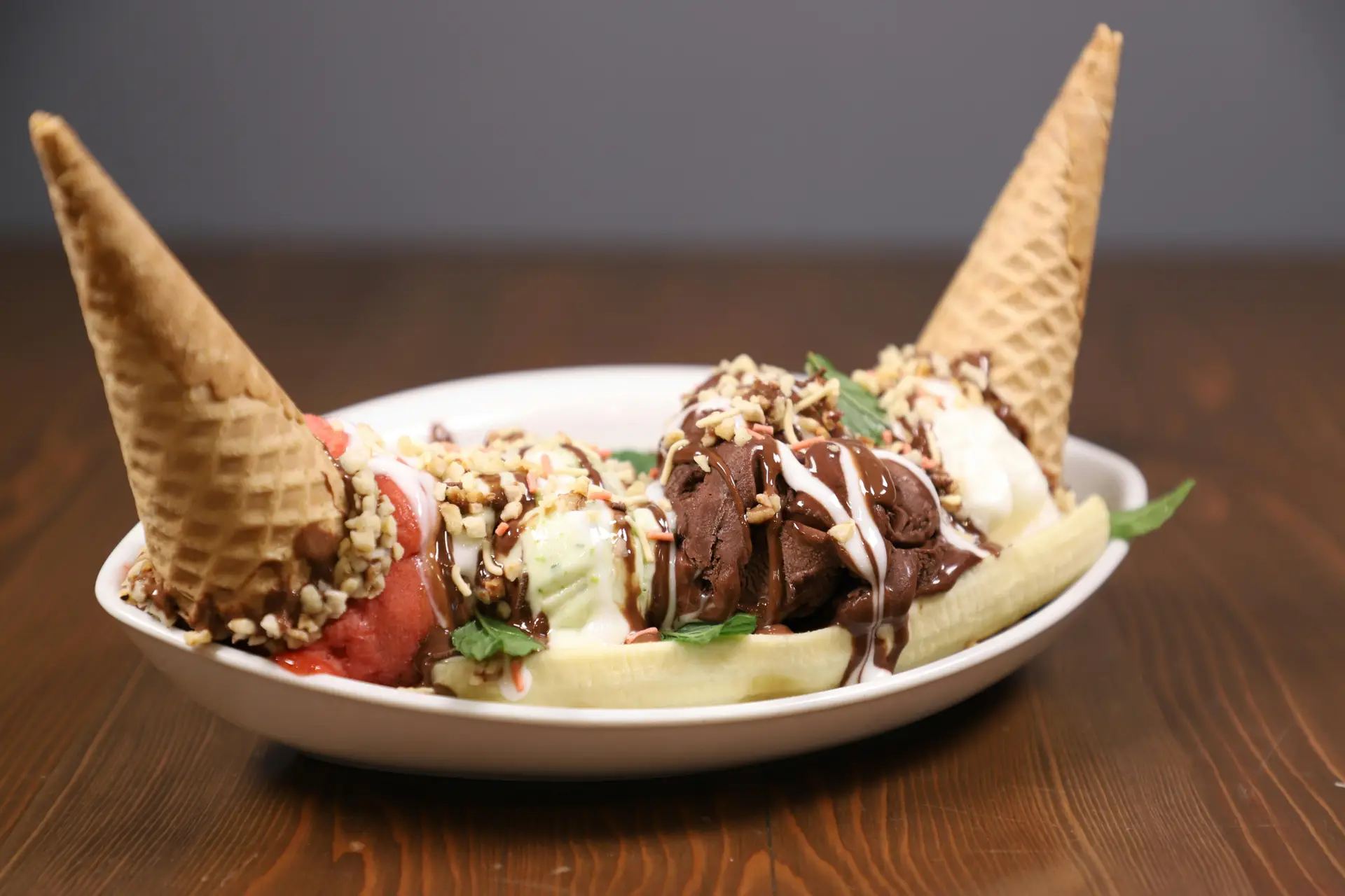 A plate of banana split with two ice cream cones, banana split, and ice cream of different flavors.