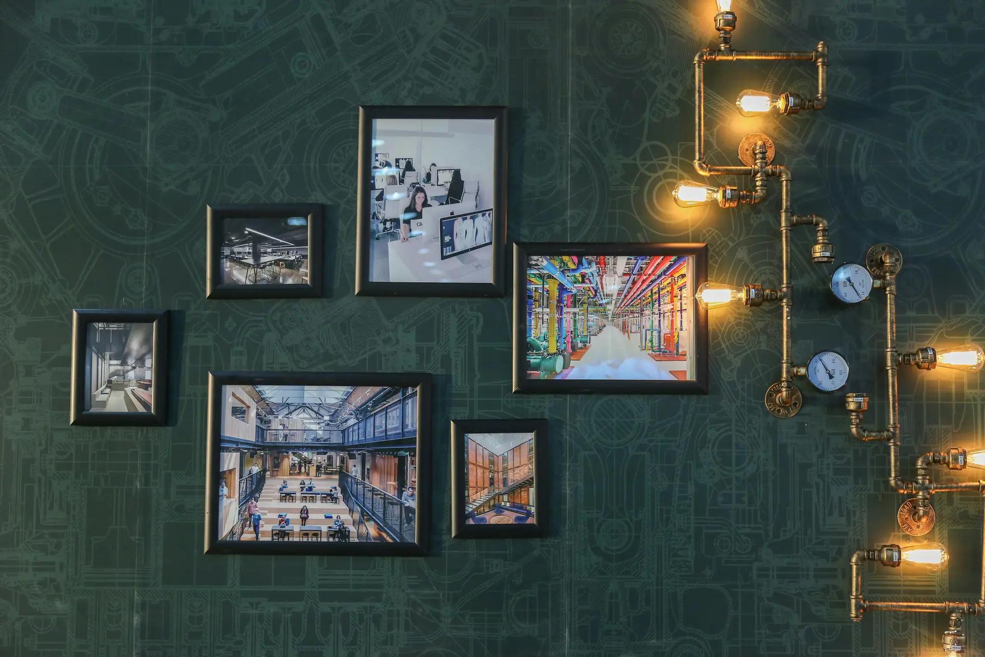 Bunch of artworks hanged on a green wall. There's artsy bulbs near them.