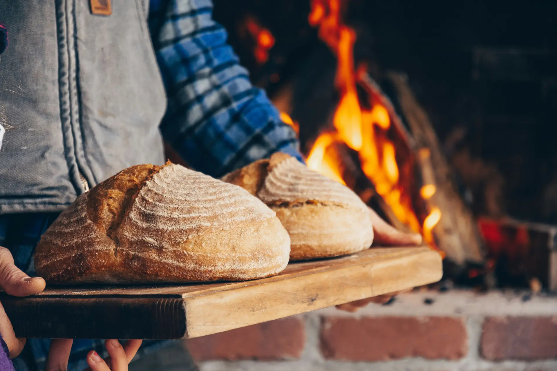A person in blue and white plaid long sleeve shirt holding bread near an oven.