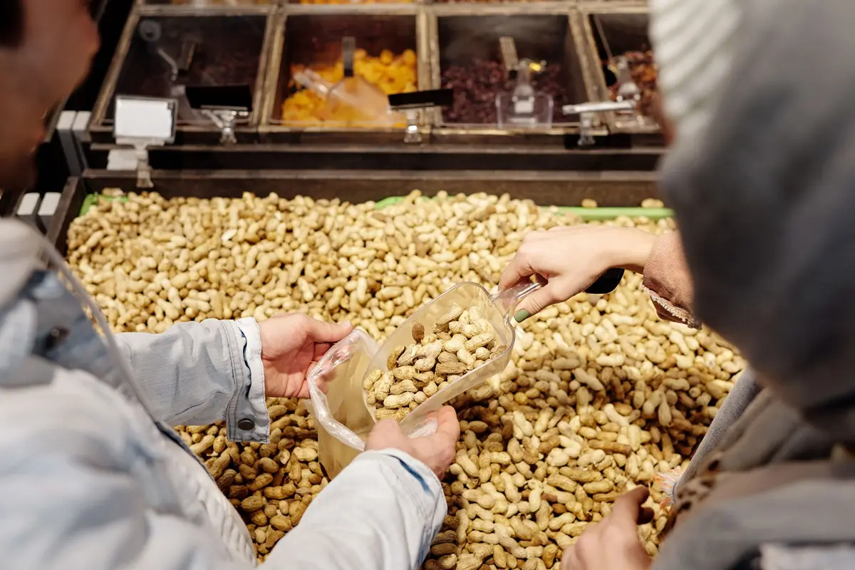 Two people buying peanuts in a supermarket using a scoop.