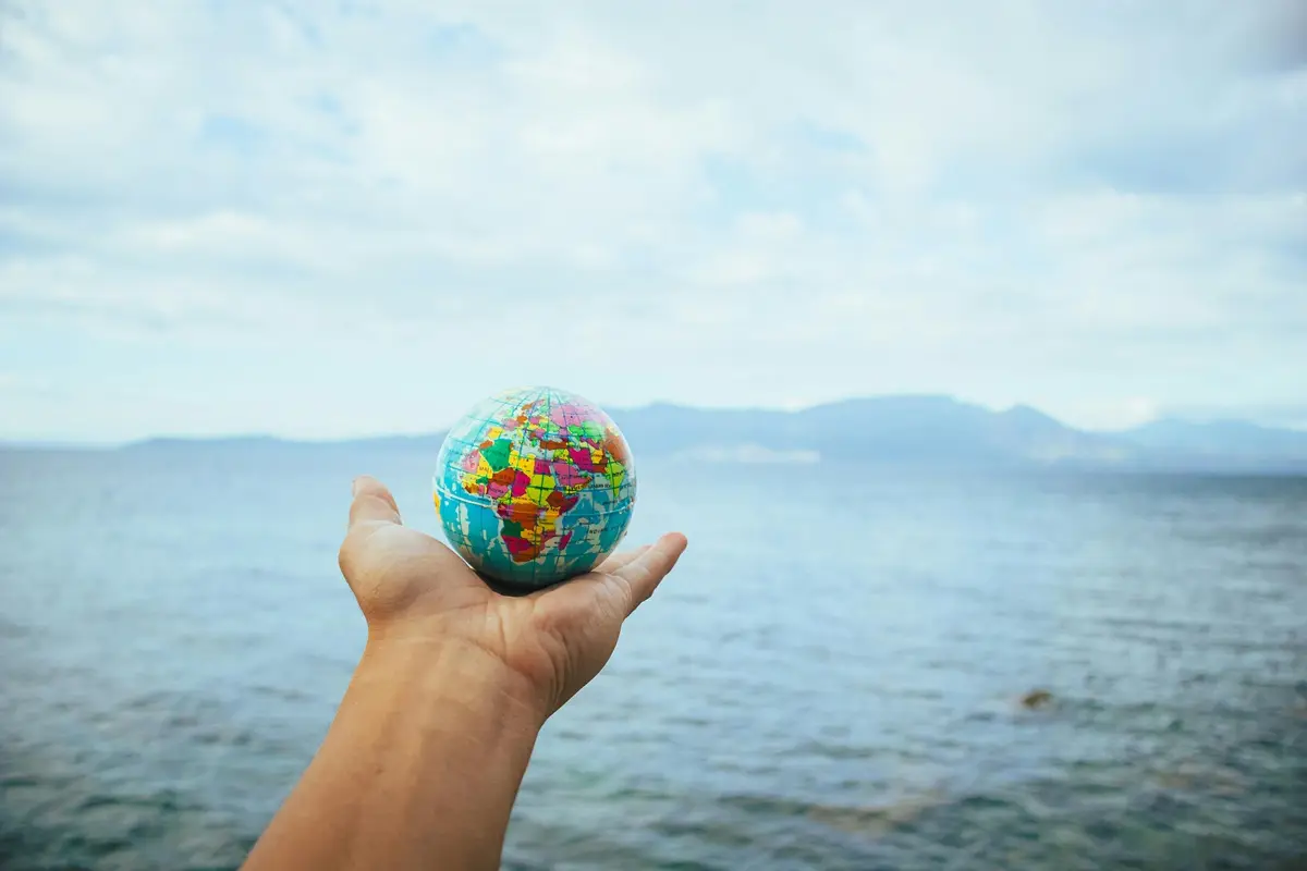A hand holds a small globe with a scenic ocean backdrop, symbolizing global exploration.