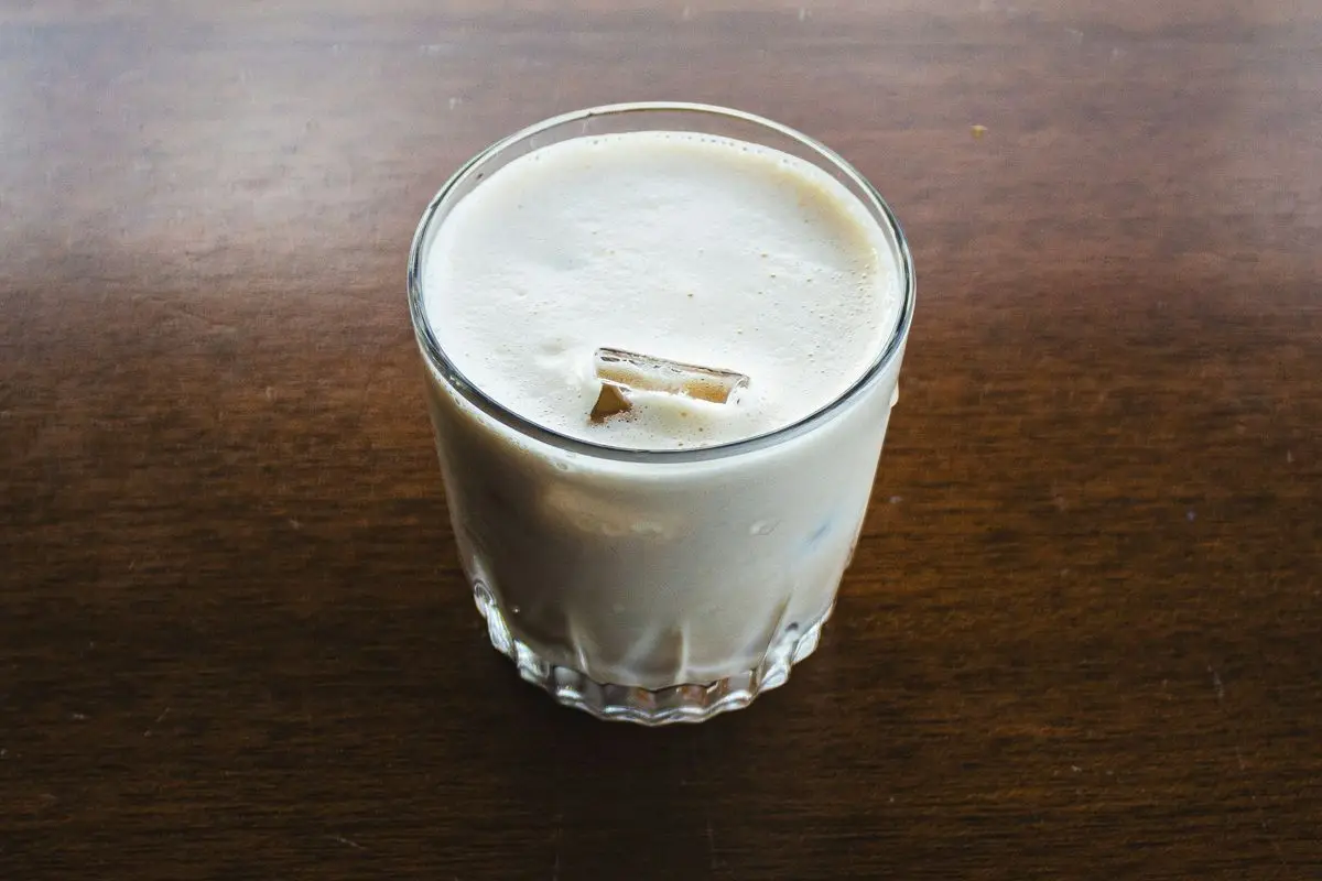 A glass of eggnog on a brown wooden table.