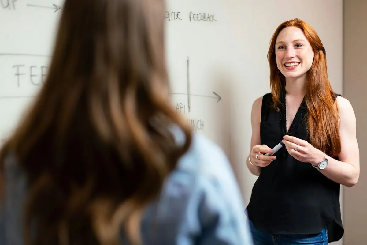 A female teacher talking to a student while standing in front of a white board.