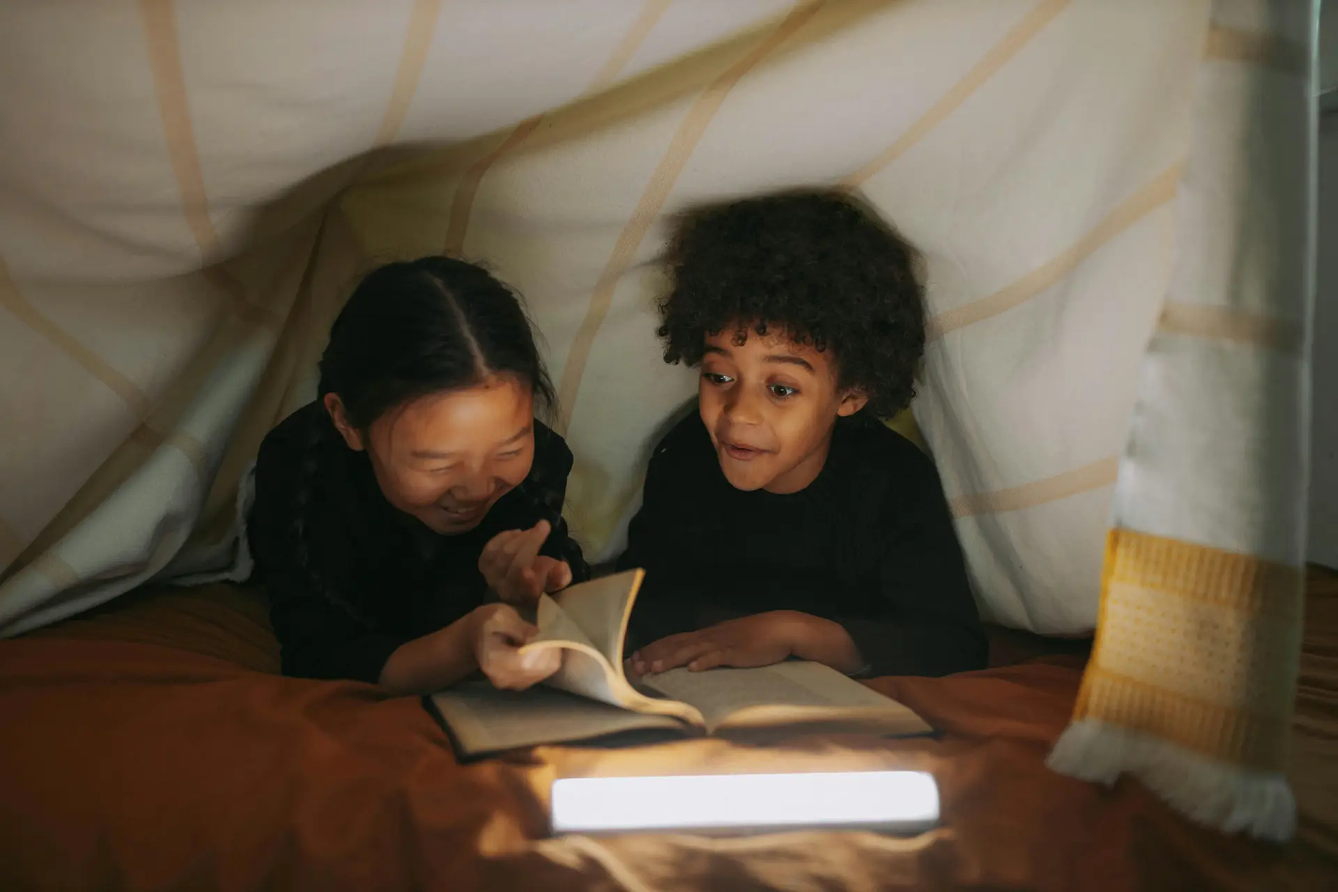 Children reading books under the blanket fort.