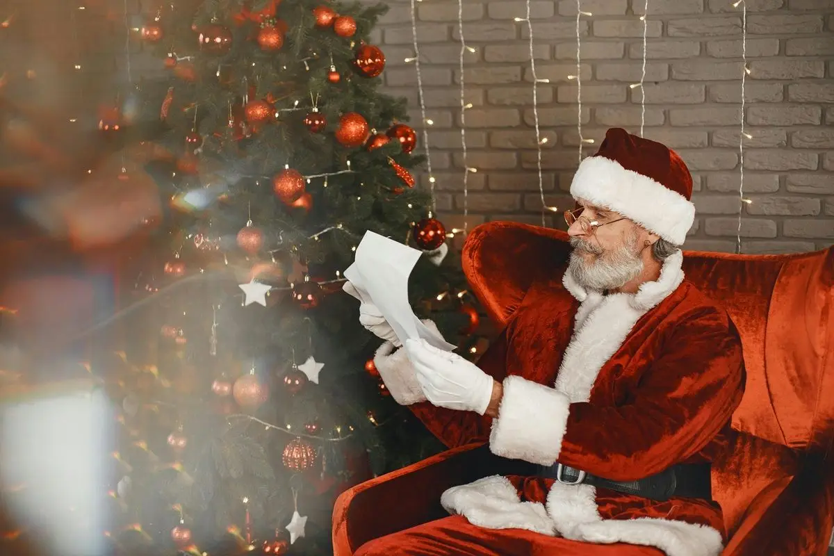 A man dressed up as Santa claus is reading a list while seating down.