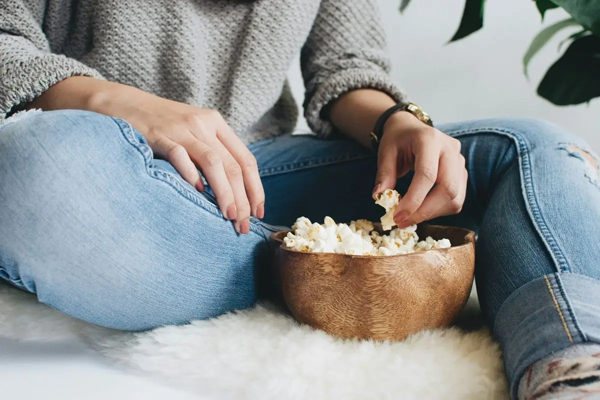 A person eating popcorn from a brown bowl while sitting on a white couch.