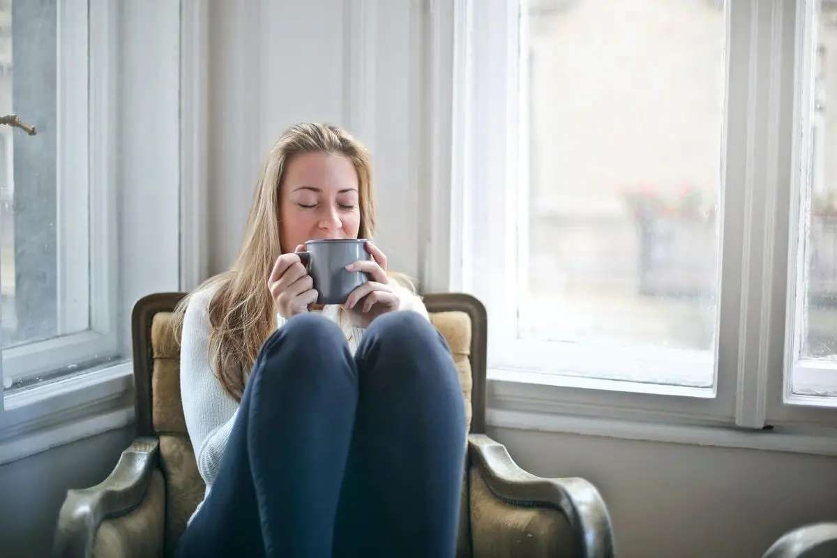 A person drinking coffee while sitting on a chair with their legs up.