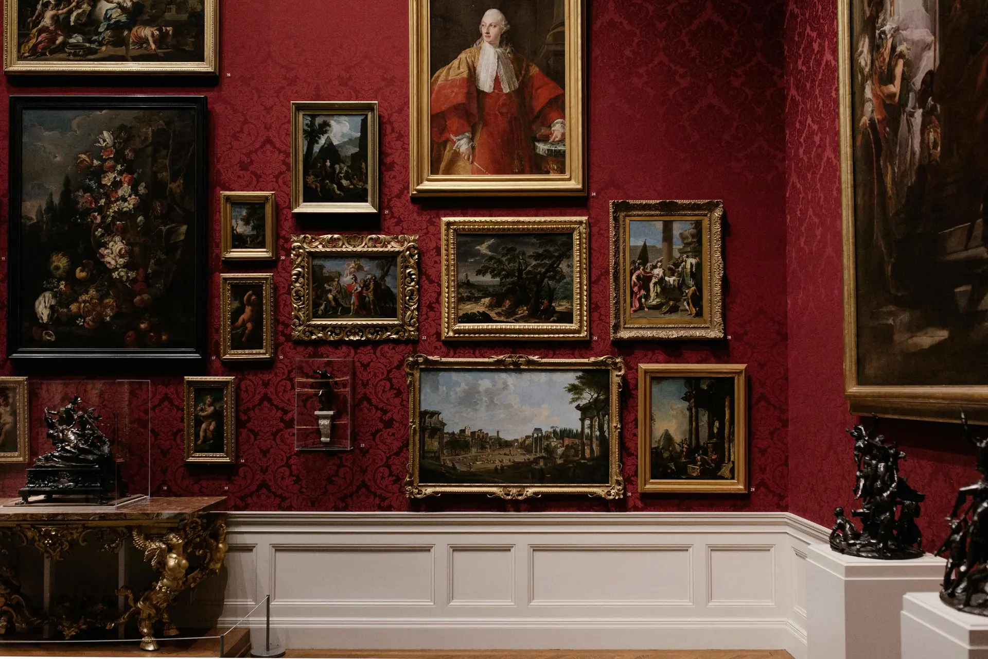 Lots of painting displayed on a red colored wall.