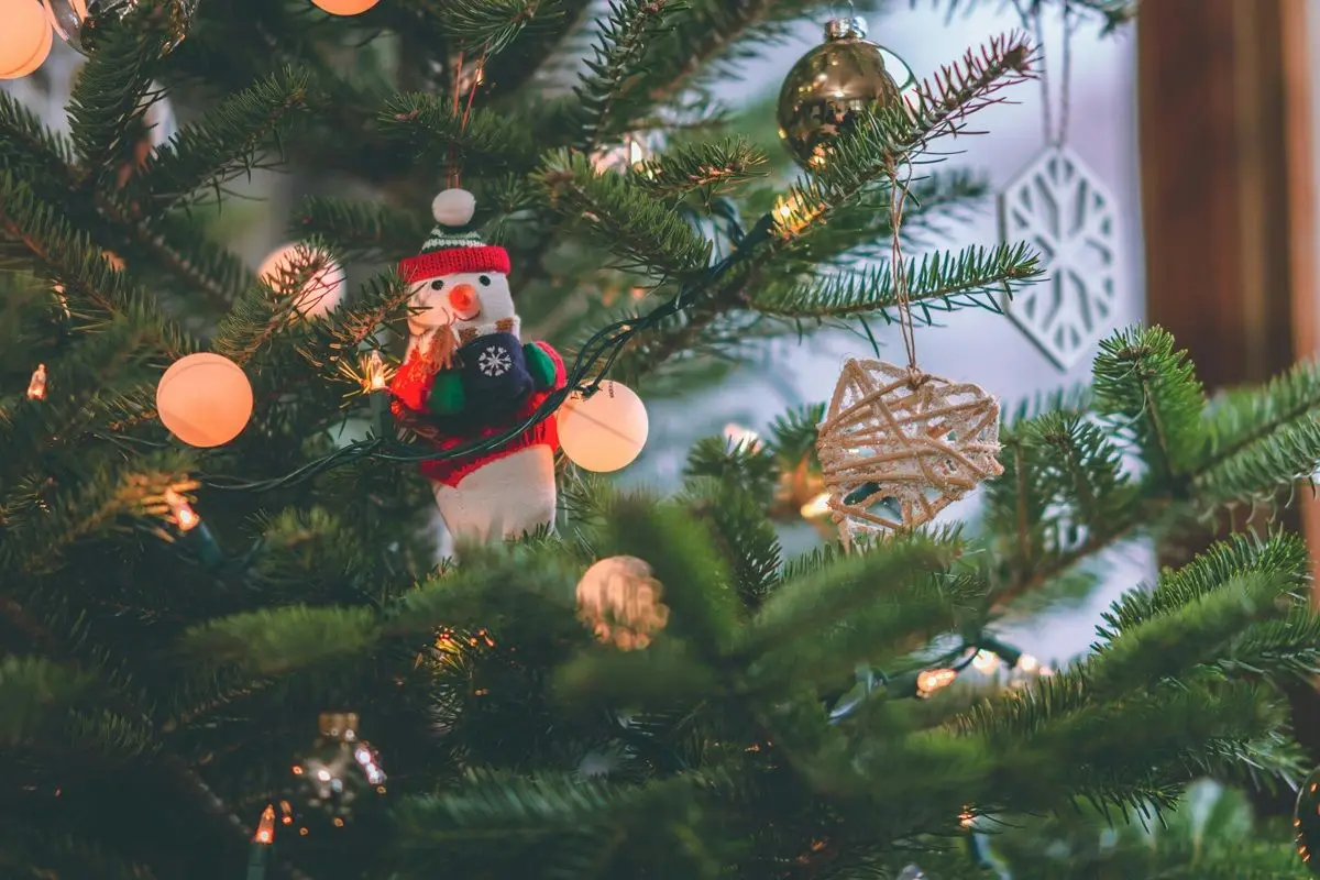 A Christmas tree decorated with different types of ornaments including lights, baubles, a snowman trinket, etc.