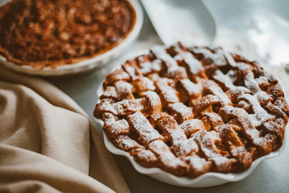 A yummy apple pie in a ceramic bowl on a wooden table next to another pie.