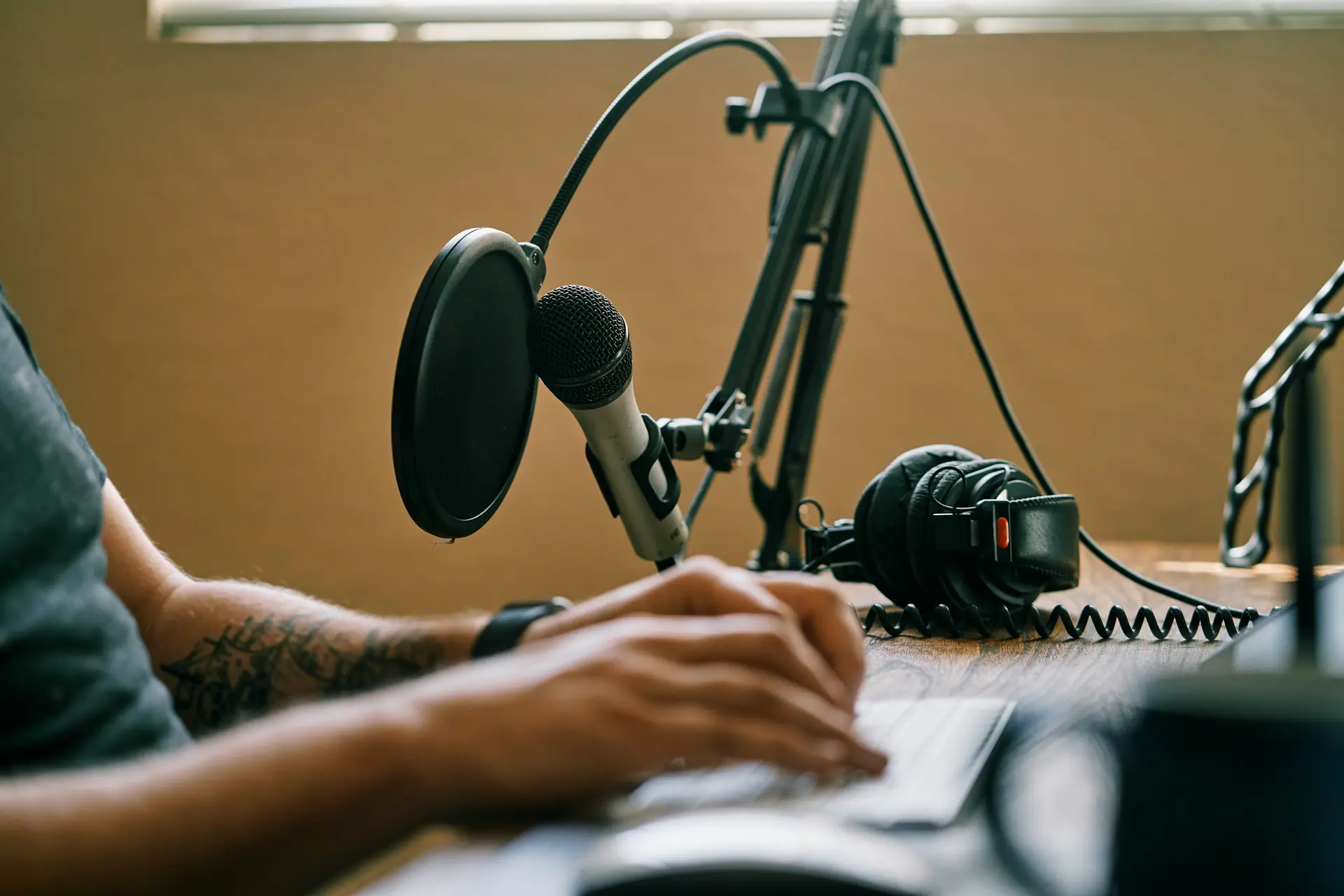 A podcaster working on his laptop which is placed on a table along with a microphone and headphone.