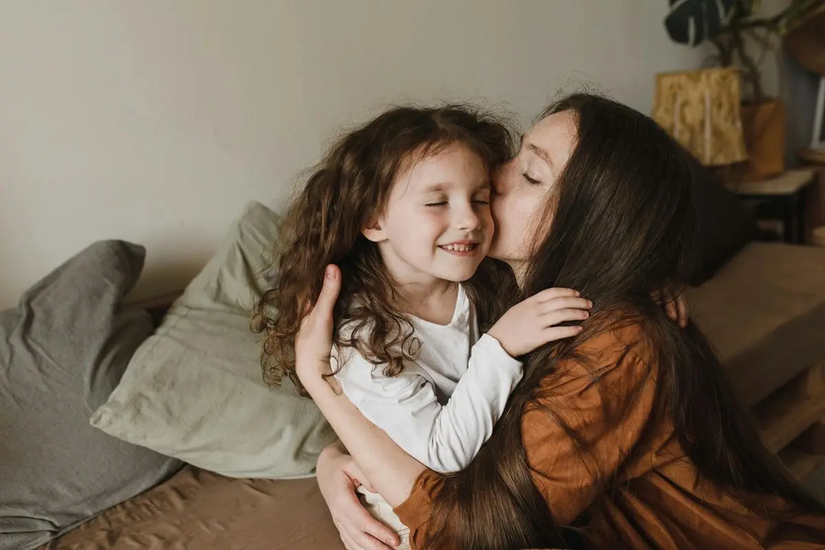 A child and her mother hugging and kissing each other.