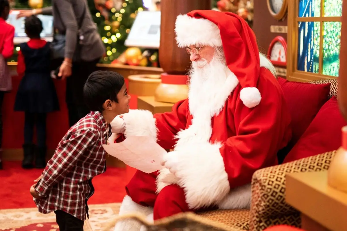 A kid talking to a man dressed up as Santa Claus.