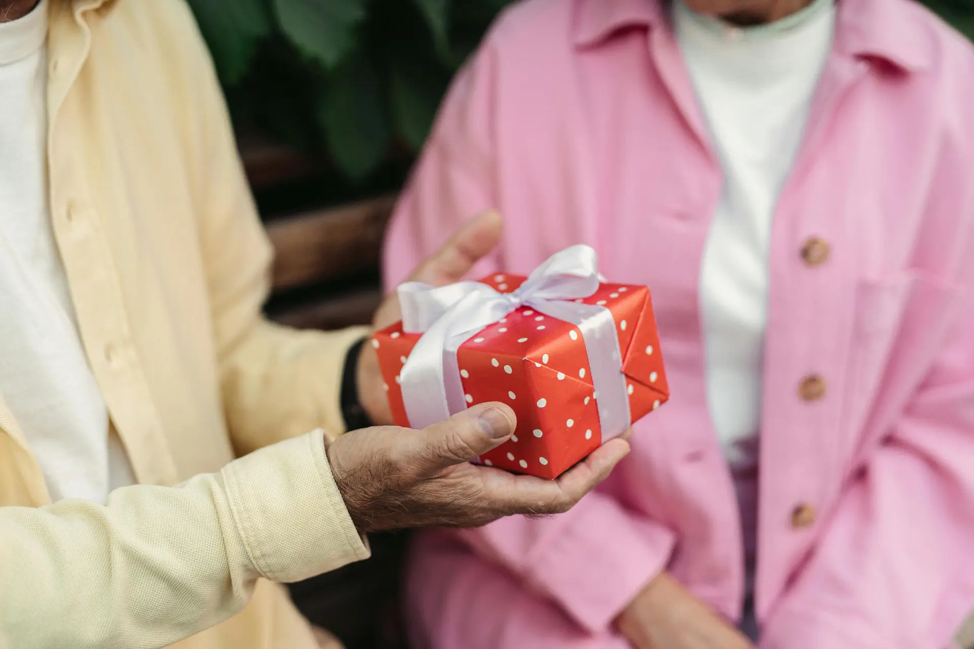 A person giving a red gift box with white bow to another person.