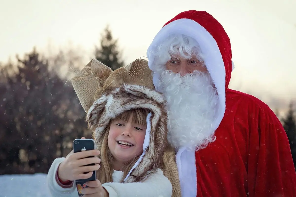 A kid taking a selfie with a man dressed up as Santa Claus.