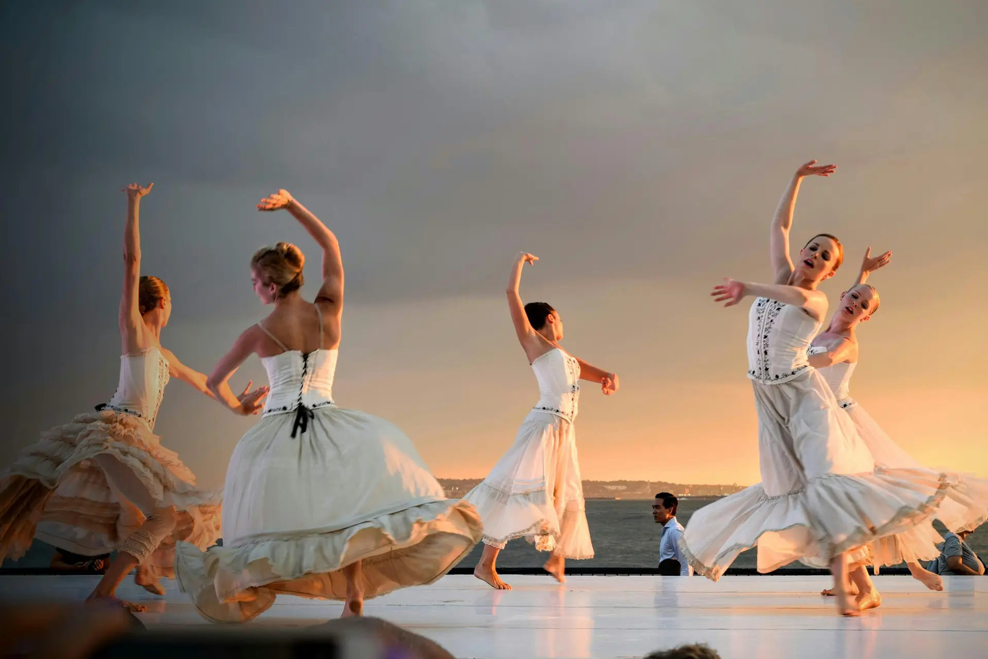 5 women in white dresses dancing in sync on the stage.