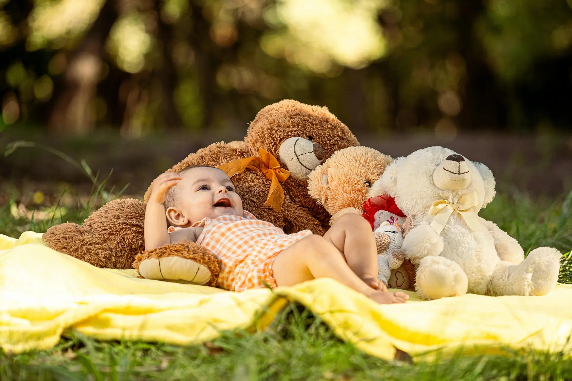 A child laying down on a yellow blanket along with few teddy bears outside.