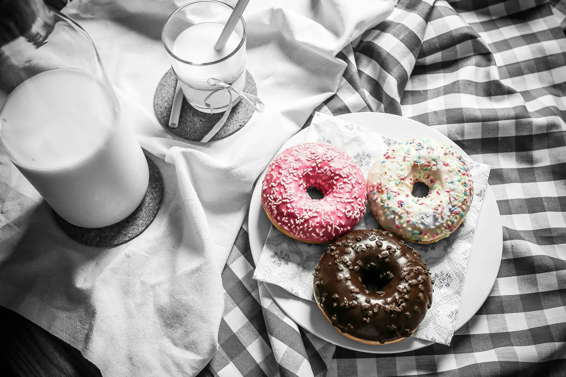 Three donut of different flavor and toppings is placed on a white ceramic plate. There's a glass of milk near the plate.
