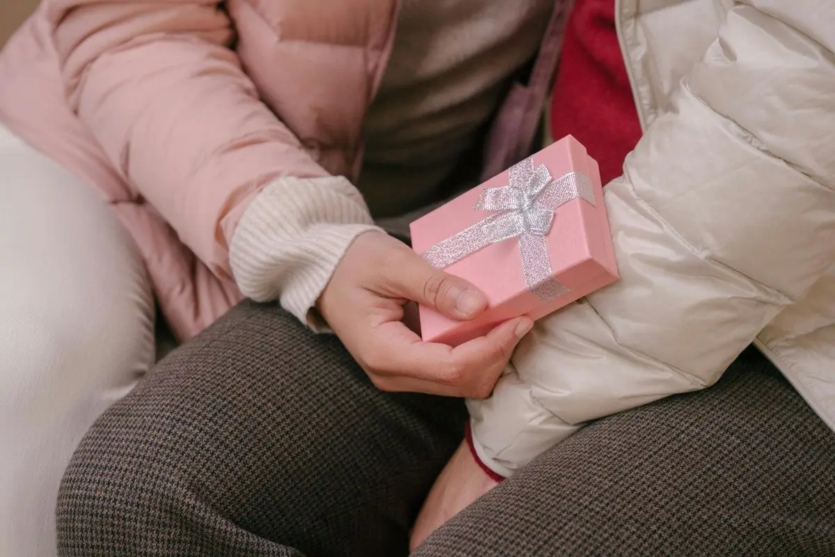 A person gifting a pink giftbox with ribbons to another person.
