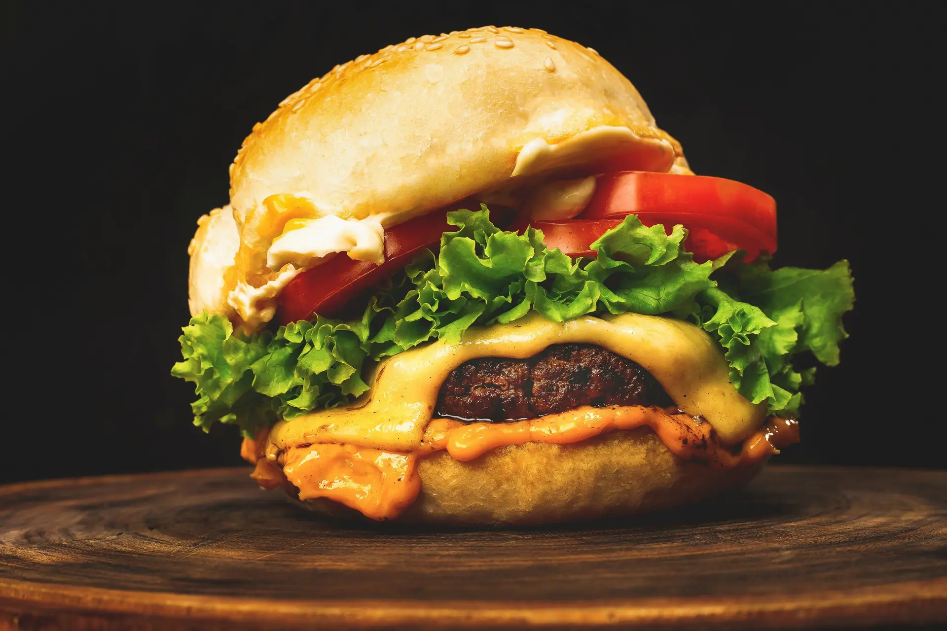 A cheeseburger with lettuce and tomato and melted cheese on a wooden surface.