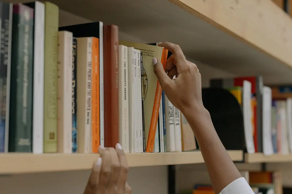 A person grabbing a book from a bookshelf filled with books.