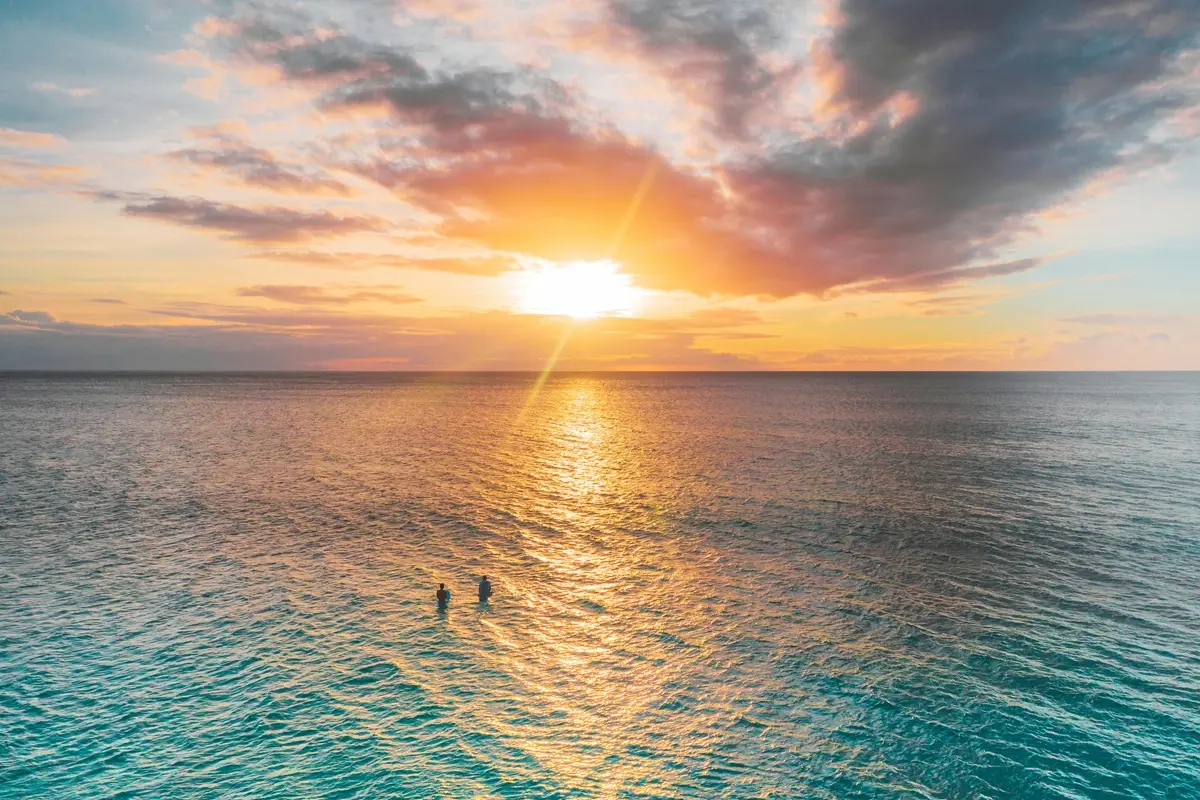 Aerial view of surfers enjoying a peaceful ocean sunrise, capturing serene seascape beauty.