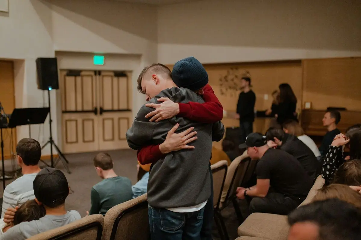 Two people hugging in a classroom which is filled with people.